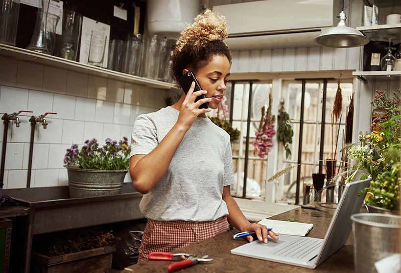 woman in kitchen talking on phone and working on laptop.
